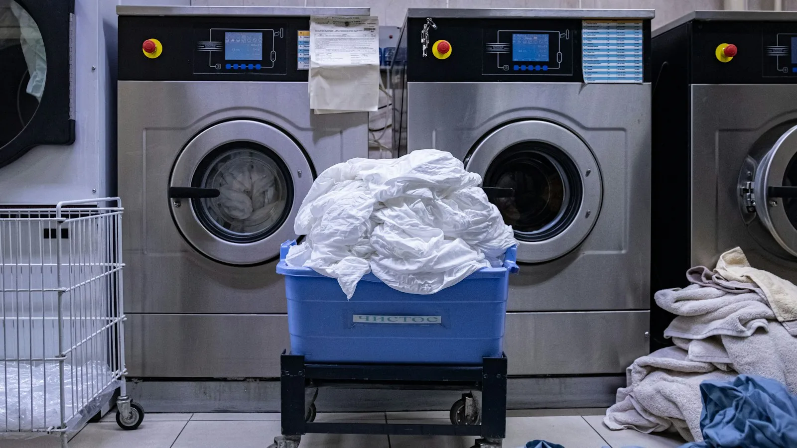 Commercial washing machines with a basket of white laundry in front