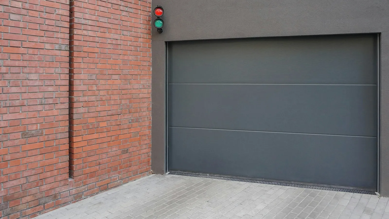 A dark grey garage door beside a brick wall with a small signal light