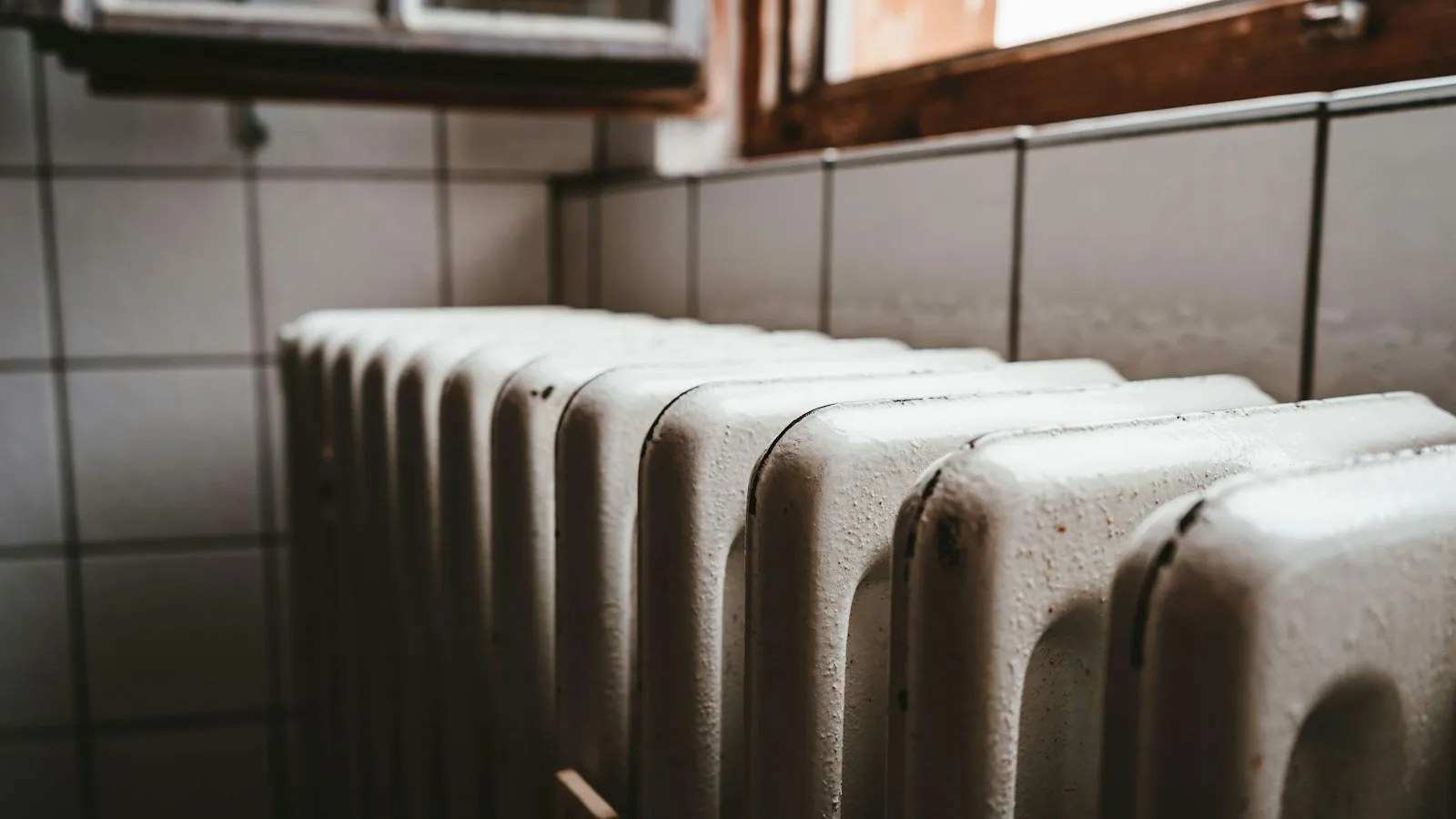 Old white cast iron radiator against a tiled wall under a window
