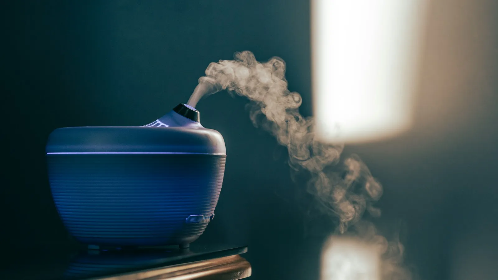 Small blue humidifier sending up a plume of mist in a dim room
