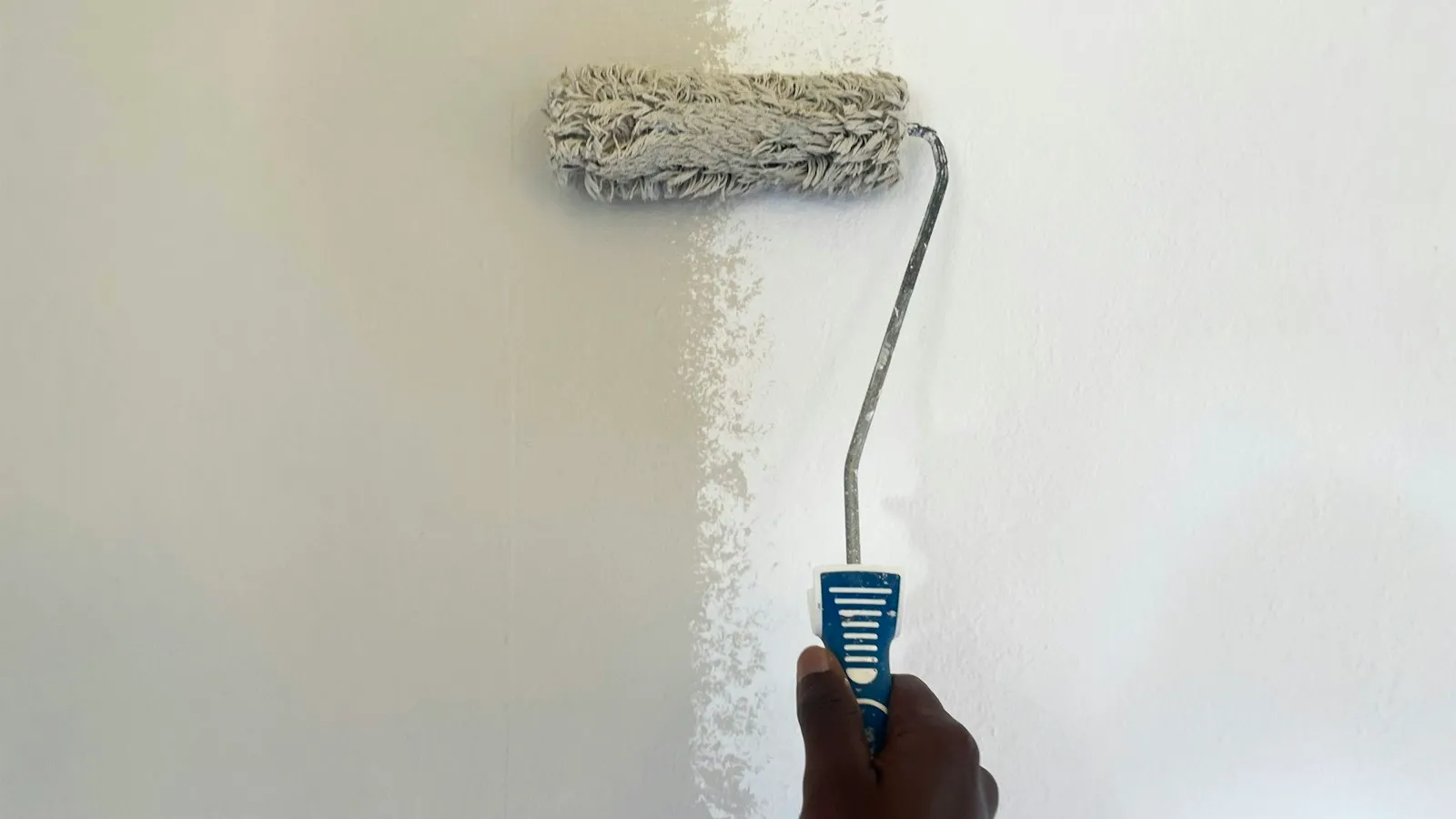 Paint roller rolling white paint onto a wall