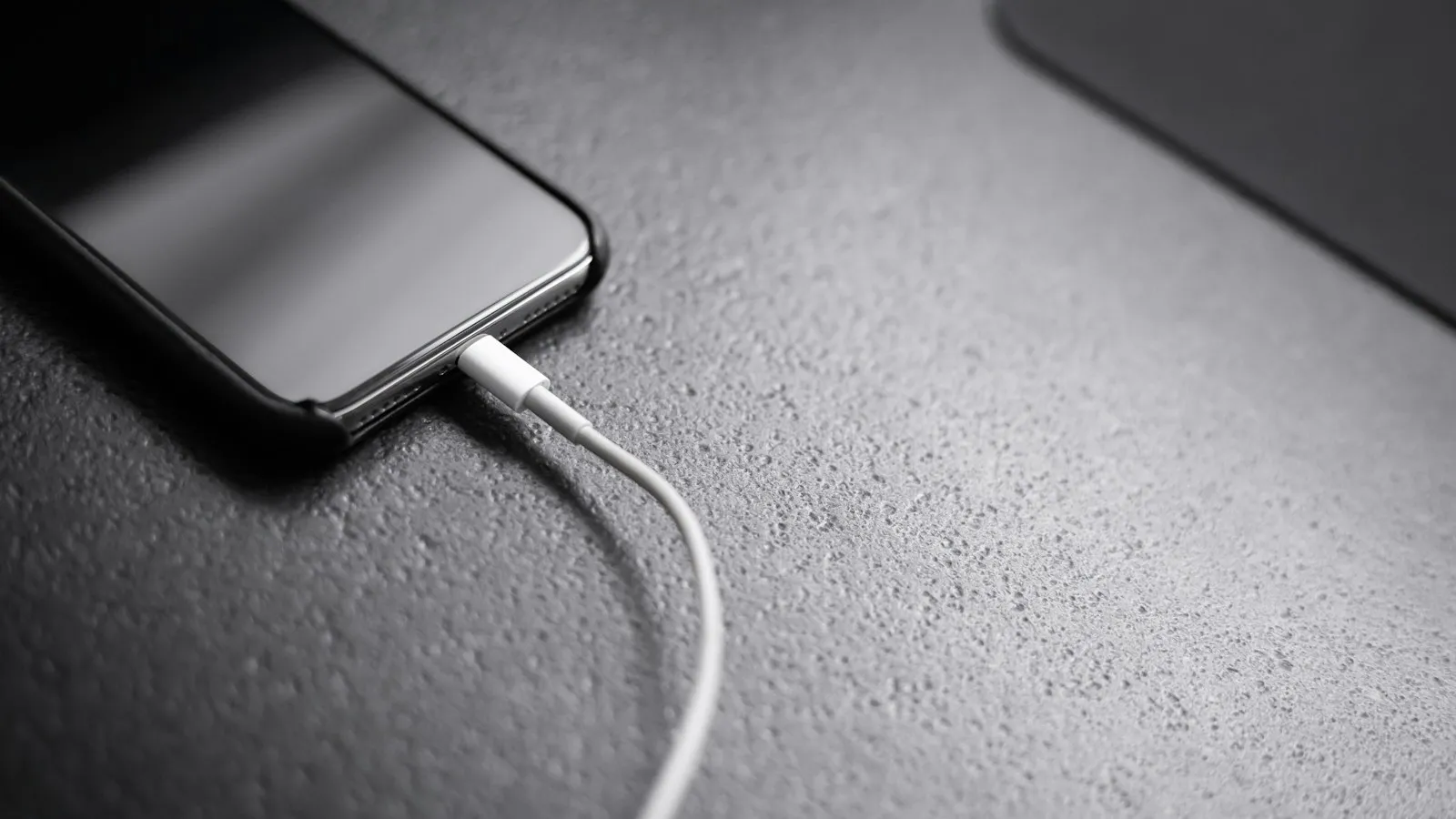 iPhone plugged into a white charging cable on a dark table