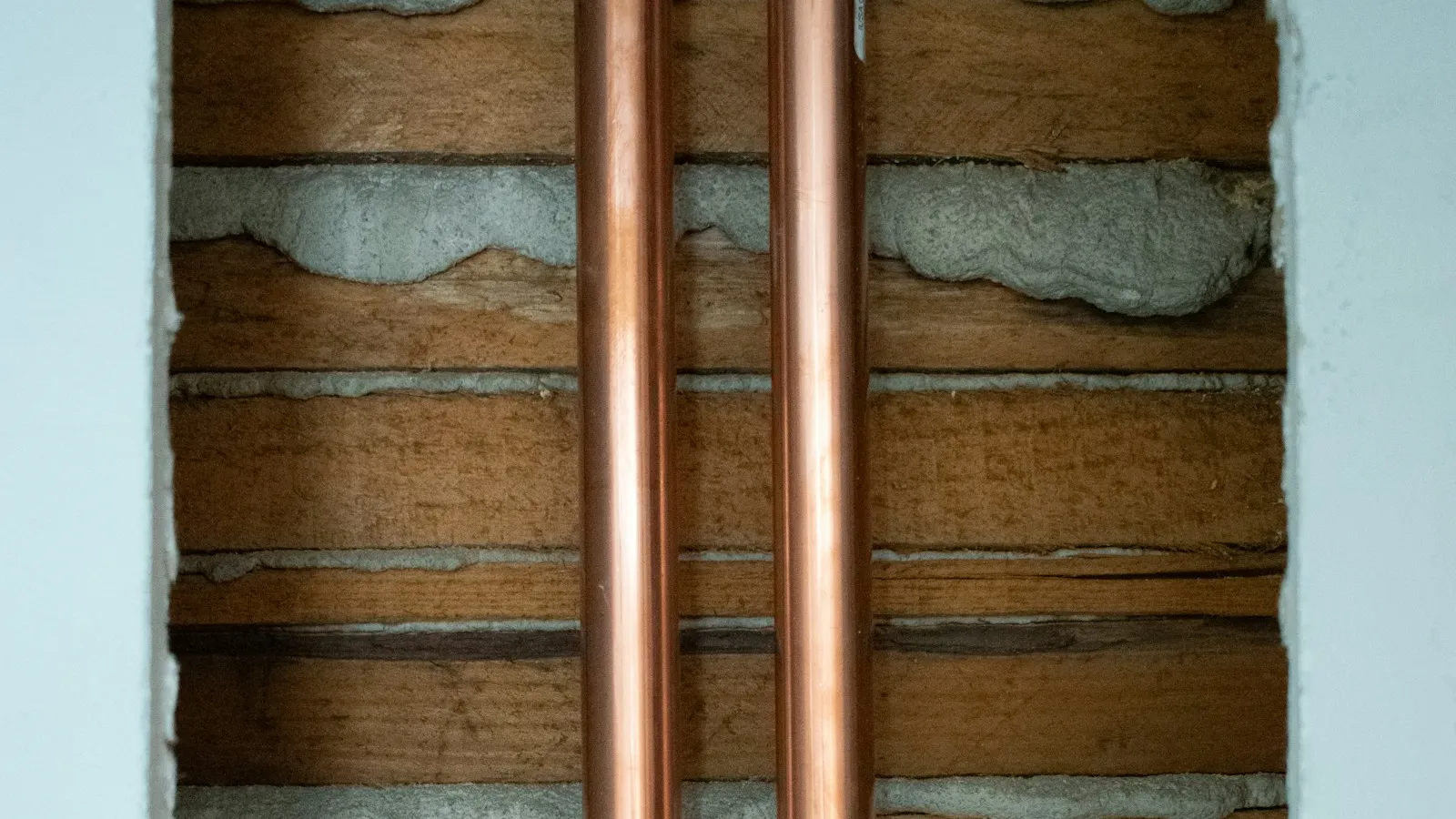 Two copper pipes running between wooden wall studs