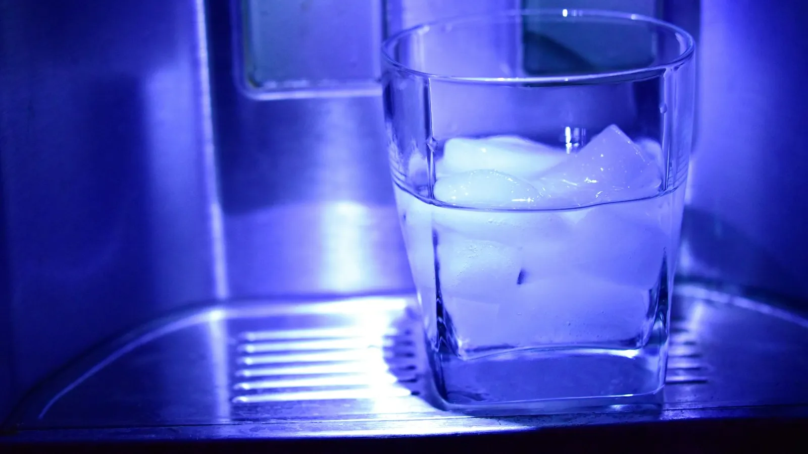 Glass of ice water under a refrigerator dispenser