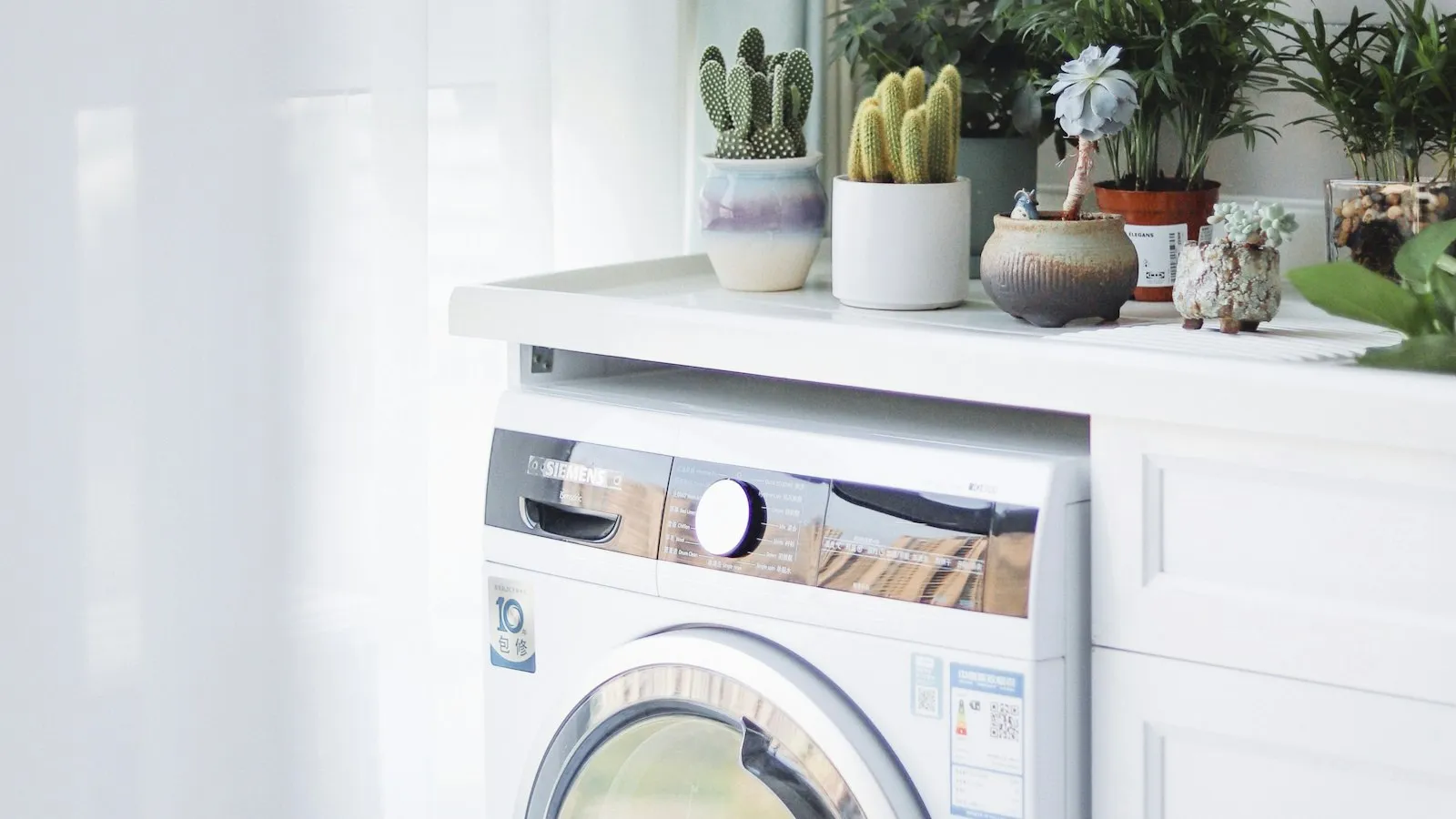 A front-load washing machine under a counter with small plants on it