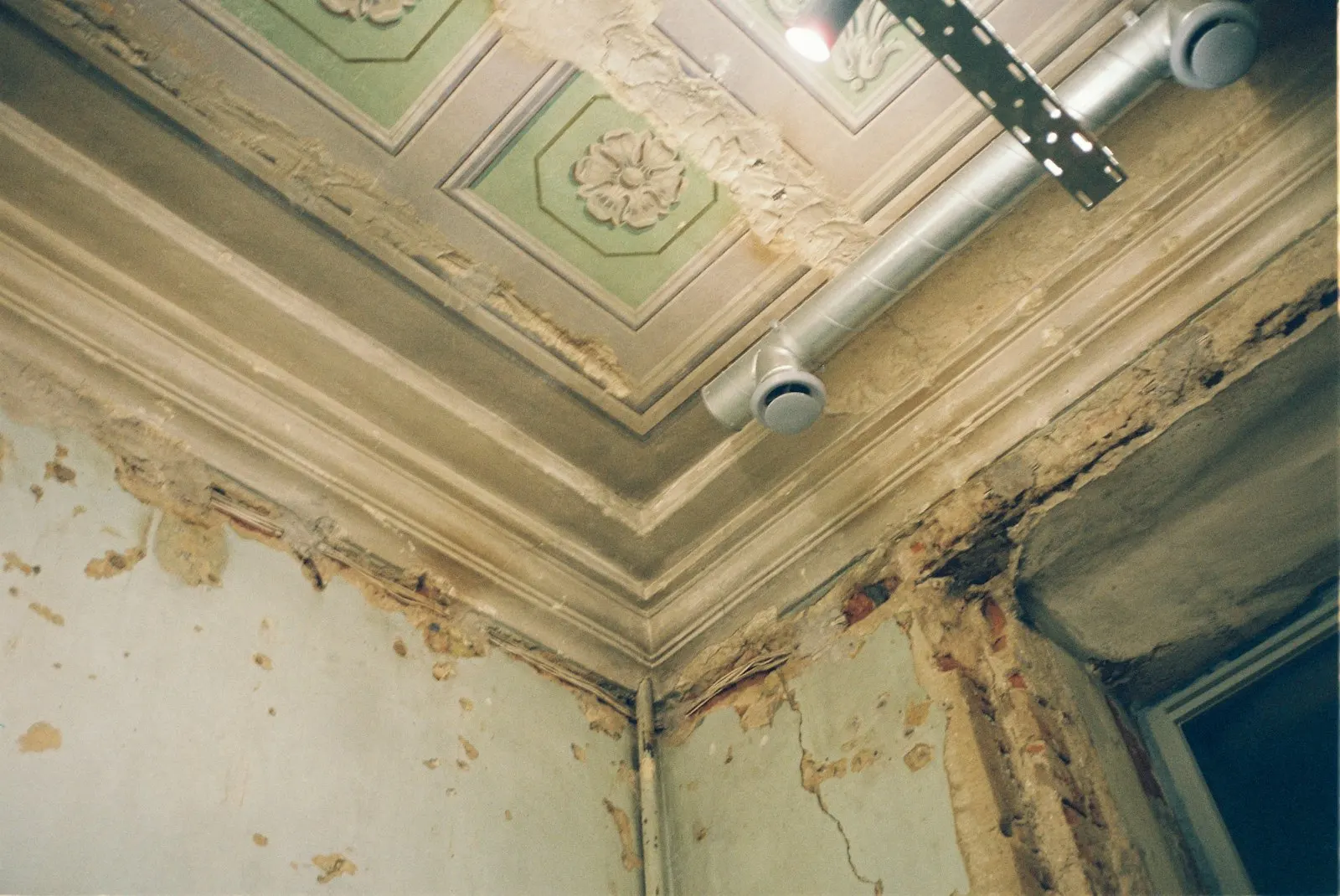 Corner of an old room with a damaged ceiling, peeling paint and flaking plaster